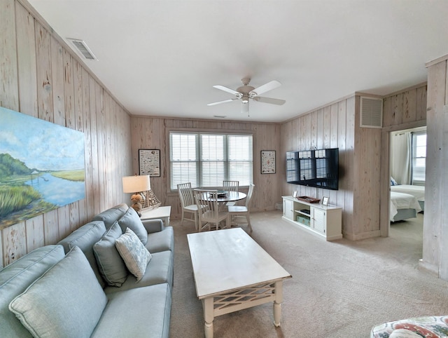 carpeted living room featuring ceiling fan and wood walls