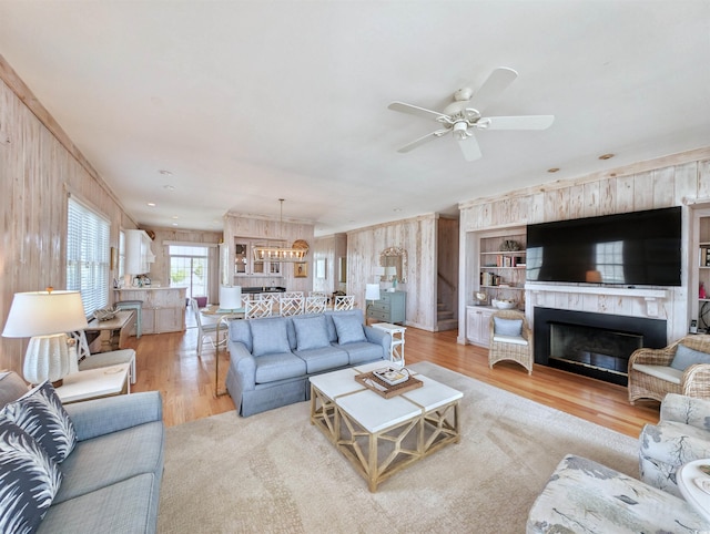 living room featuring wood walls, ceiling fan with notable chandelier, and light hardwood / wood-style flooring