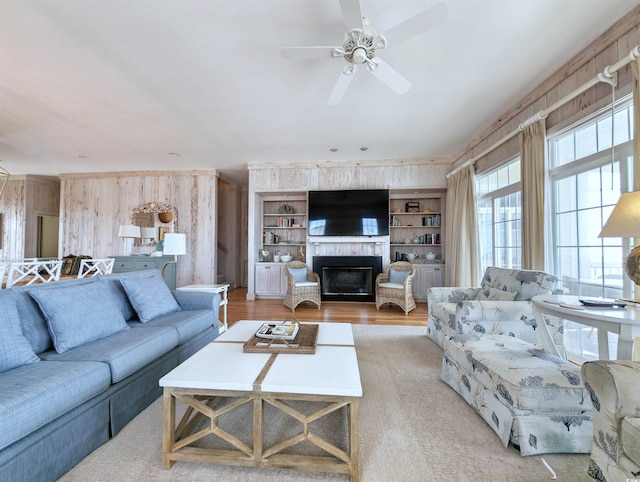 living room featuring built in shelves, light hardwood / wood-style flooring, wood walls, and ceiling fan