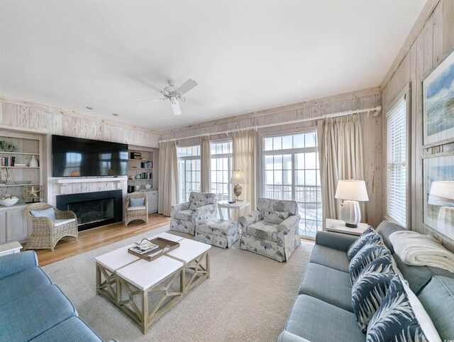 living room featuring built in features, ceiling fan, and wood walls