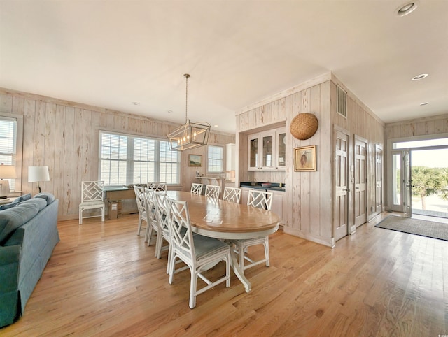 dining area with a wealth of natural light, wood walls, a chandelier, and light hardwood / wood-style floors