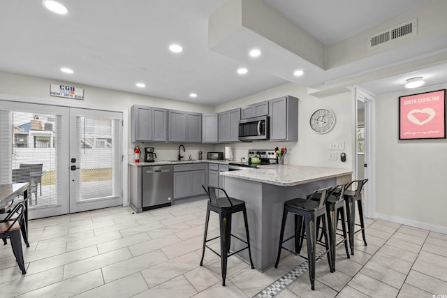 kitchen featuring gray cabinetry, a kitchen bar, stainless steel appliances, sink, and light stone counters