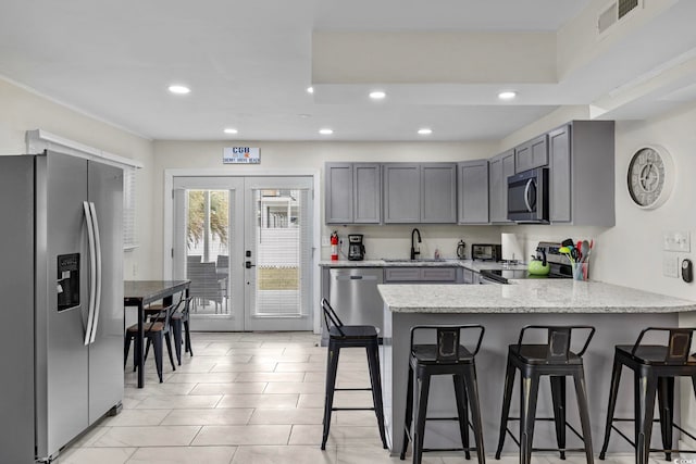 kitchen with french doors, light stone counters, stainless steel appliances, kitchen peninsula, and a kitchen breakfast bar