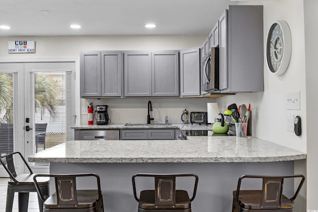 kitchen with appliances with stainless steel finishes, light stone counters, a breakfast bar area, and gray cabinetry