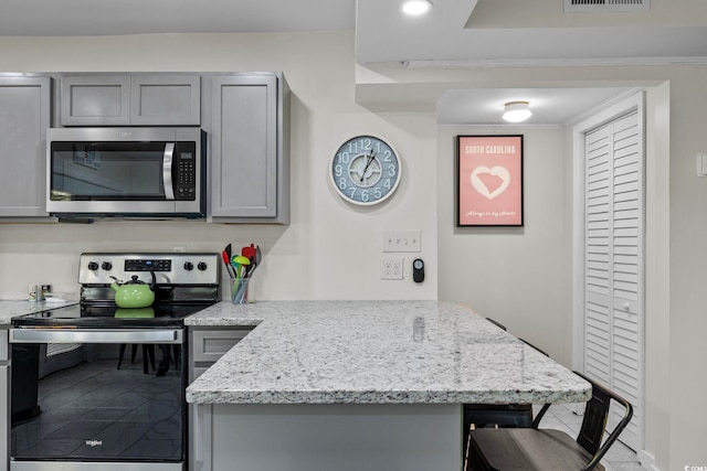 kitchen with gray cabinets, a kitchen bar, stainless steel appliances, and light stone countertops