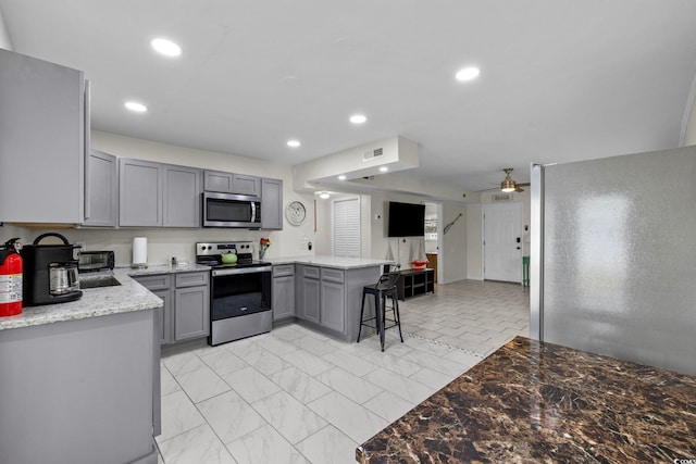 kitchen featuring gray cabinetry, appliances with stainless steel finishes, ceiling fan, kitchen peninsula, and a kitchen breakfast bar