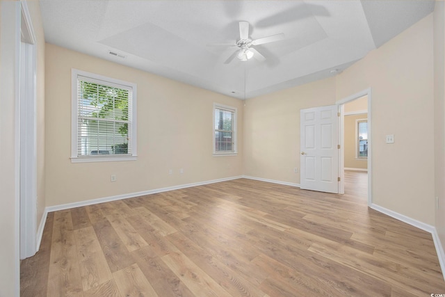 unfurnished room with light wood-type flooring, ceiling fan, and a raised ceiling