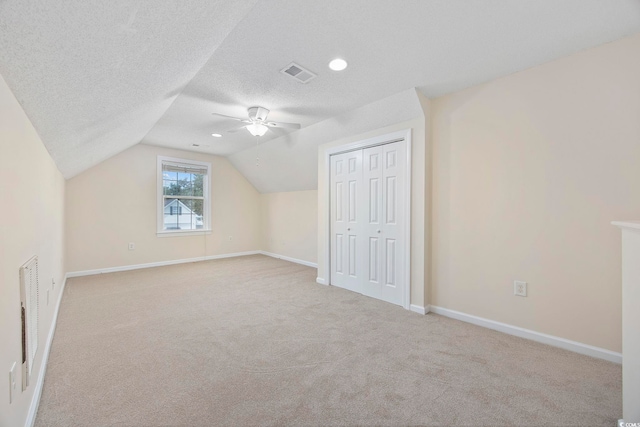 additional living space with vaulted ceiling, light colored carpet, ceiling fan, and a textured ceiling