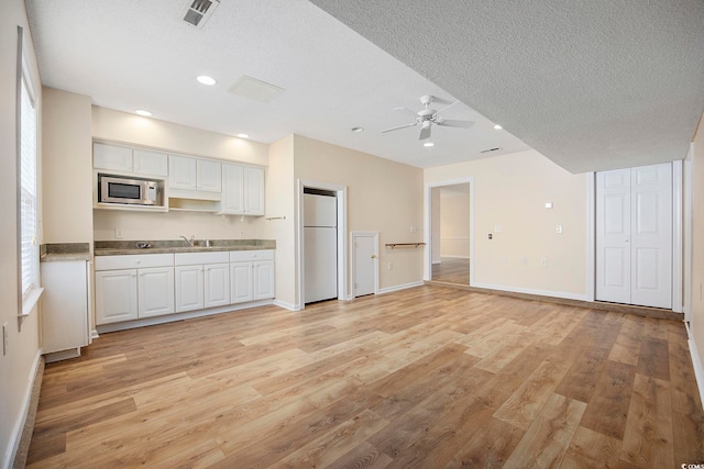 kitchen with ceiling fan, stainless steel microwave, white refrigerator, and white cabinets