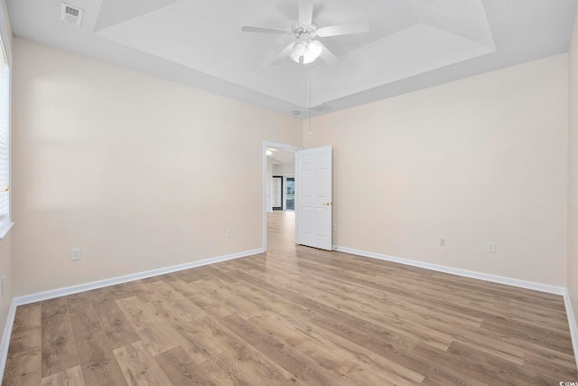 spare room featuring a tray ceiling, ceiling fan, and light hardwood / wood-style flooring