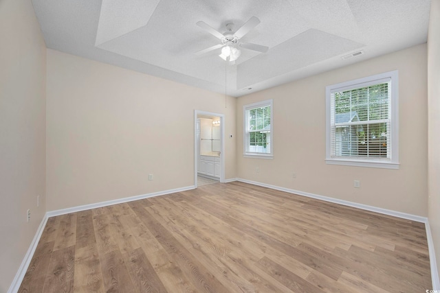 empty room with light wood-type flooring, a textured ceiling, a tray ceiling, and ceiling fan