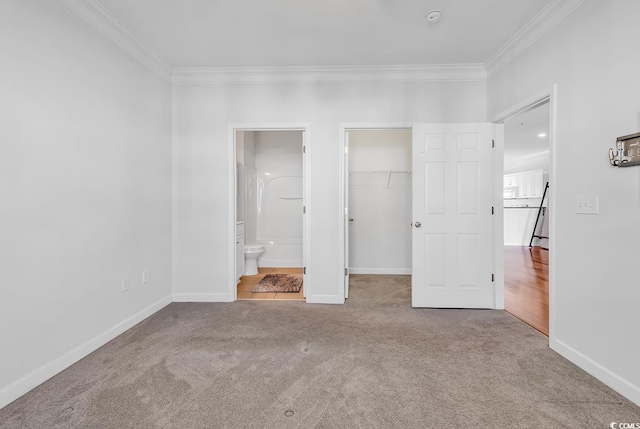 unfurnished bedroom with crown molding, a closet, a spacious closet, light carpet, and ensuite bath