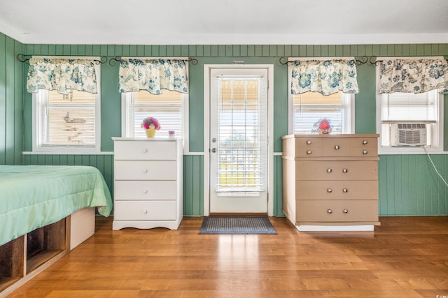 unfurnished bedroom featuring access to exterior, light hardwood / wood-style floors, cooling unit, and wooden walls