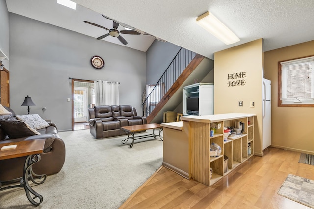 living room with ceiling fan, vaulted ceiling, a textured ceiling, and light hardwood / wood-style flooring