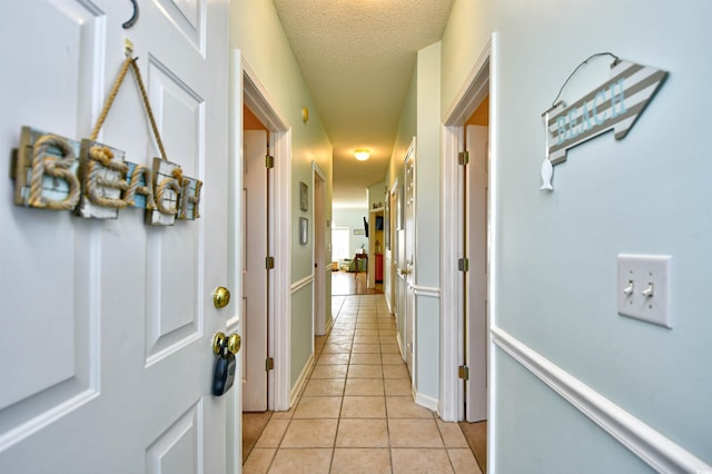 hall with a textured ceiling and light tile patterned floors