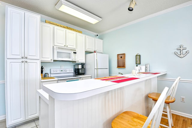 kitchen with white appliances, ornamental molding, a kitchen bar, and white cabinetry