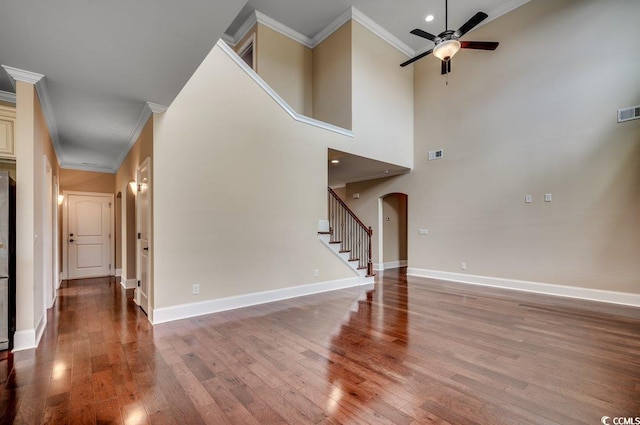 unfurnished living room with ornamental molding, ceiling fan, a towering ceiling, and wood-type flooring