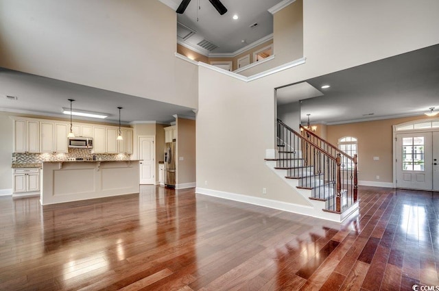 unfurnished living room featuring a high ceiling, ornamental molding, wood-type flooring, and ceiling fan with notable chandelier