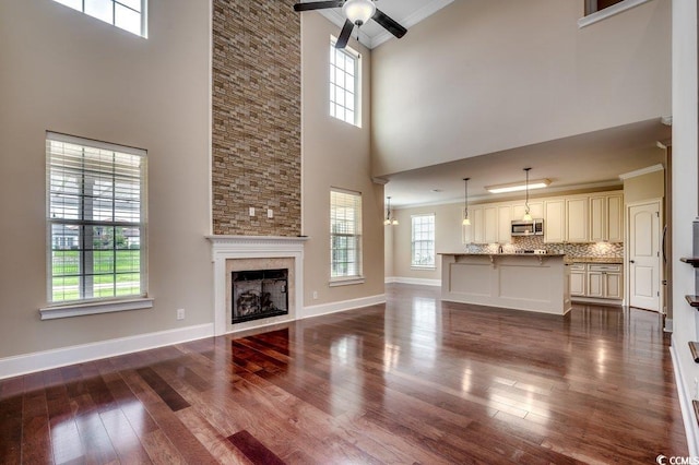 unfurnished living room with hardwood / wood-style floors, a wealth of natural light, a towering ceiling, and ornamental molding