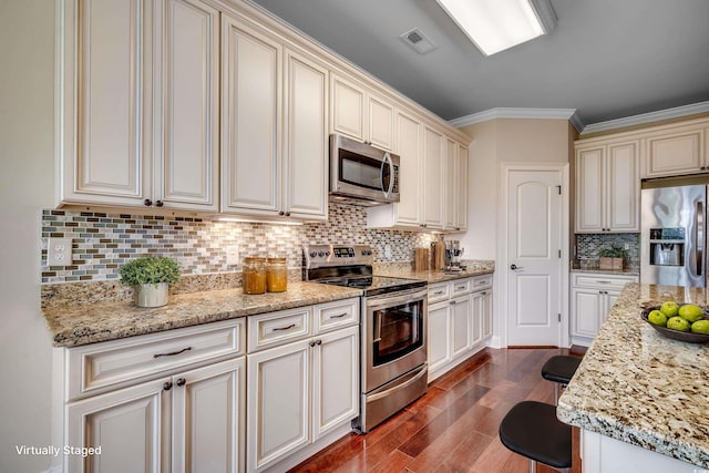 kitchen featuring wood-type flooring, backsplash, light stone countertops, ornamental molding, and appliances with stainless steel finishes