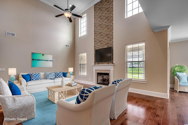 living room with a high ceiling, a healthy amount of sunlight, a stone fireplace, and dark hardwood / wood-style floors