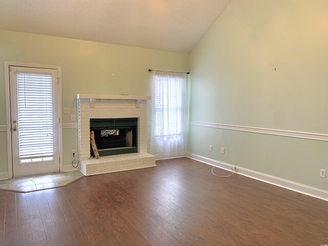 unfurnished living room featuring vaulted ceiling, a brick fireplace, a wealth of natural light, and dark hardwood / wood-style floors