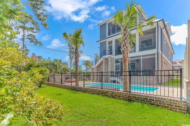 back of property with a fenced in pool, a sunroom, and a lawn