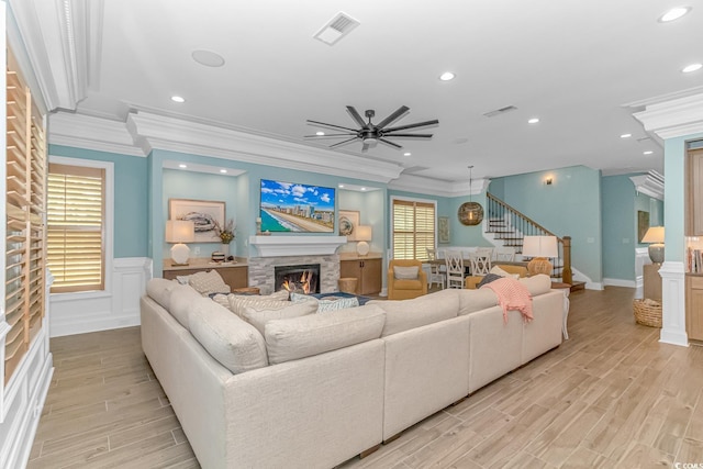 living room with ceiling fan, ornamental molding, a stone fireplace, and light wood-type flooring