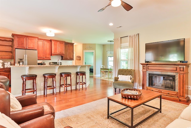 living area featuring a glass covered fireplace, ceiling fan, light wood-style flooring, and baseboards