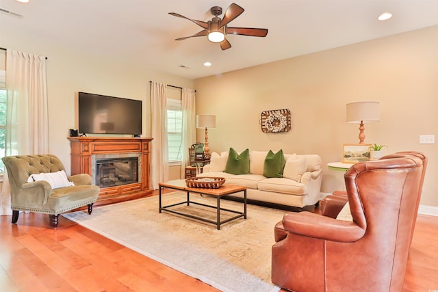 living area with a glass covered fireplace, wood finished floors, visible vents, and a ceiling fan