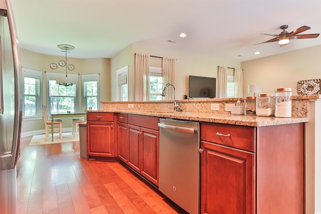 kitchen with light stone counters, light wood-style flooring, stainless steel appliances, a sink, and decorative light fixtures