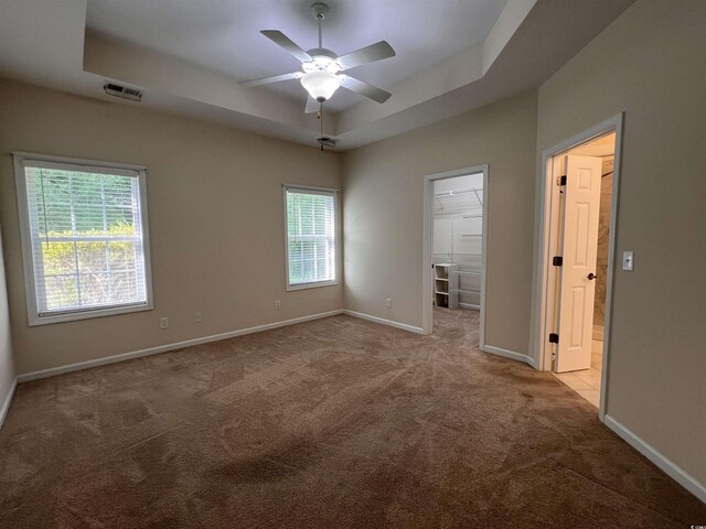 empty room featuring ceiling fan, a raised ceiling, and light colored carpet