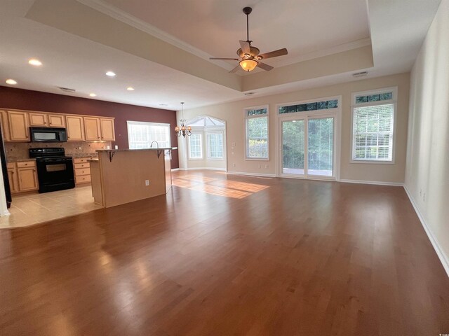 unfurnished living room featuring light tile patterned floors, a wealth of natural light, ceiling fan with notable chandelier, and a tray ceiling