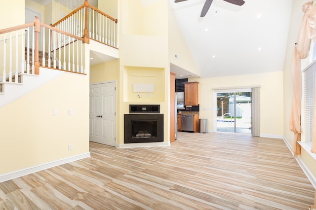 unfurnished living room featuring a high ceiling, a ceiling fan, baseboards, stairs, and light wood finished floors