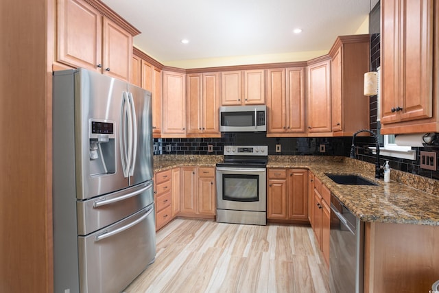 kitchen with decorative backsplash, dark stone counters, stainless steel appliances, light wood-type flooring, and a sink