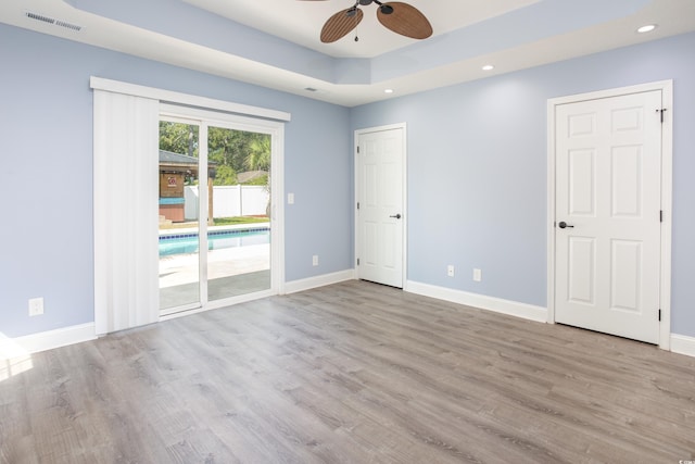 spare room with baseboards, visible vents, a raised ceiling, and wood finished floors