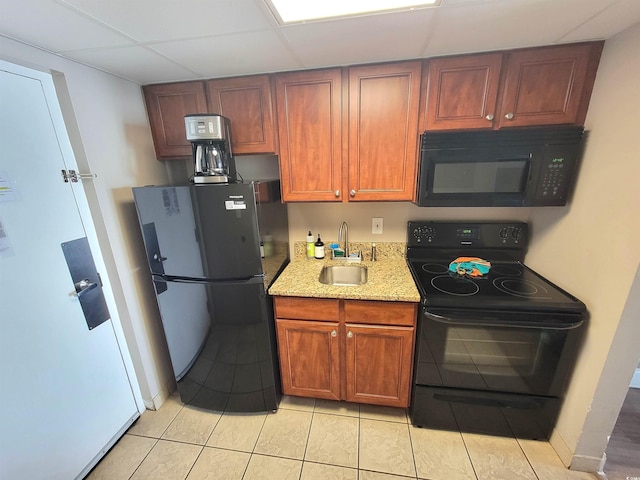 kitchen with sink, light tile patterned floors, black appliances, light stone countertops, and a drop ceiling