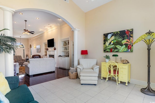 tiled living room featuring crown molding, decorative columns, ceiling fan, and a high ceiling