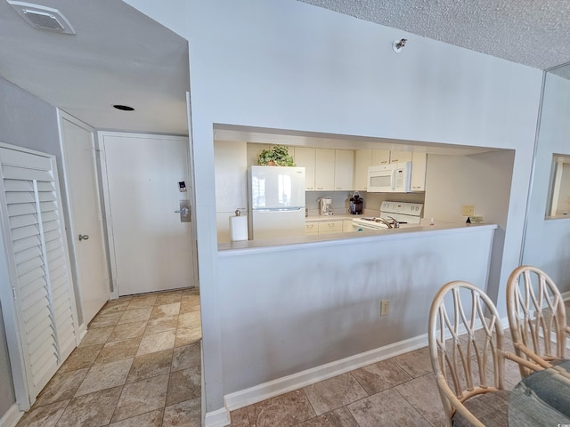 kitchen with a textured ceiling, white appliances, white cabinetry, and kitchen peninsula