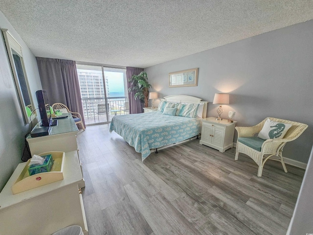 bedroom featuring a textured ceiling, access to outside, light hardwood / wood-style floors, and floor to ceiling windows