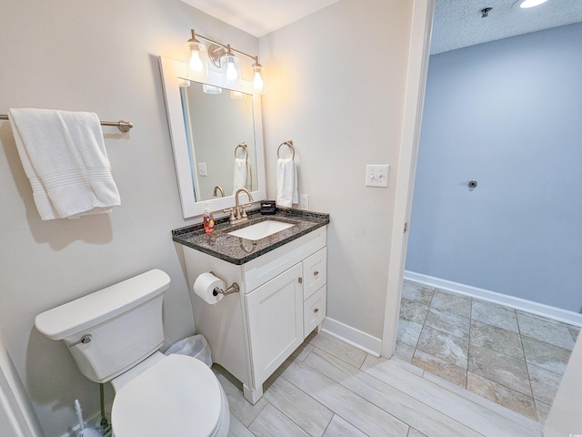 bathroom with a textured ceiling, vanity, and toilet