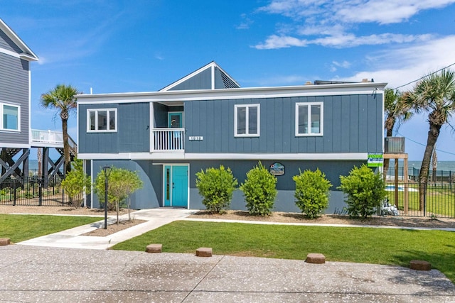 raised beach house with a balcony, fence, a front lawn, and concrete driveway