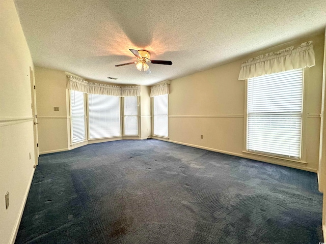 empty room with a textured ceiling, ceiling fan, and dark carpet