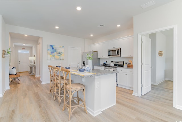 kitchen featuring stainless steel appliances, white cabinetry, light hardwood / wood-style floors, and an island with sink