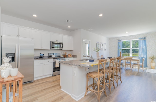 kitchen with a center island with sink, white cabinets, sink, appliances with stainless steel finishes, and light hardwood / wood-style floors