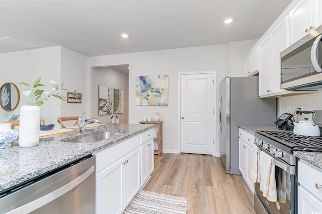 kitchen featuring sink, light stone counters, light hardwood / wood-style flooring, white cabinets, and appliances with stainless steel finishes