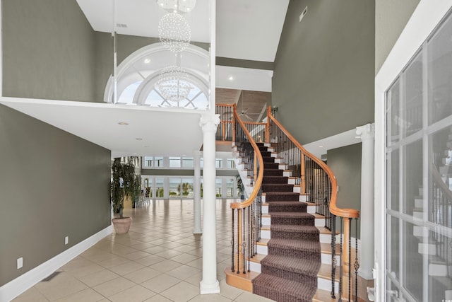 tiled foyer featuring a high ceiling, decorative columns, and a notable chandelier