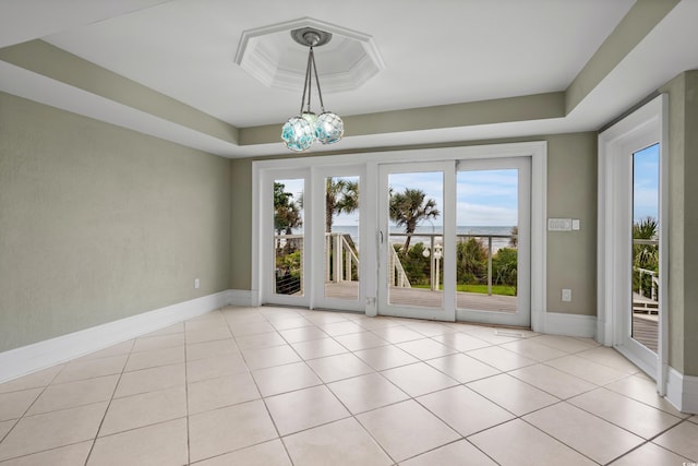 tiled empty room featuring an inviting chandelier and a tray ceiling