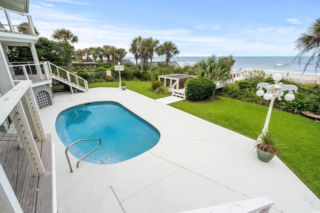 view of pool with a patio, a water view, a yard, and a beach view