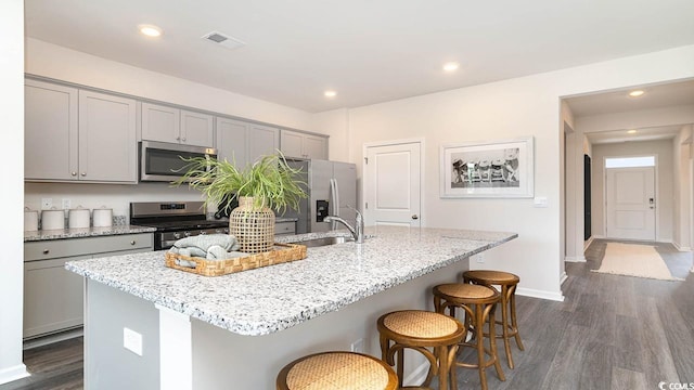kitchen with a center island with sink, gray cabinetry, dark wood-type flooring, and appliances with stainless steel finishes